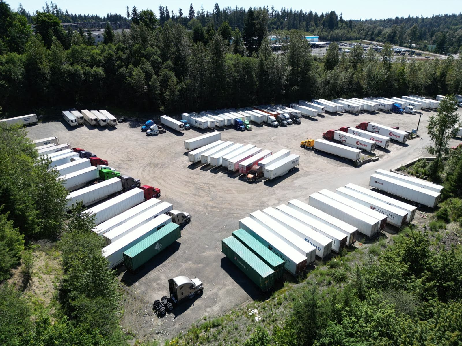 Aerial view of the Flame Truck Parking yard on Witte Rd SE in Maple Valley, Washington: rows of trailers and tractors parked on gravel, ringed by trees.